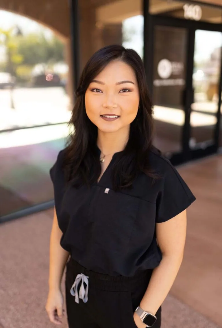 A woman wearing a black scrubs, standing in front of a glass wall with one of her hand in the pocket.