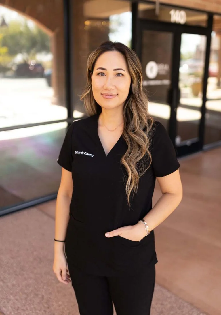 A woman standing in front of a glass wall with one of her hand in the pocket.