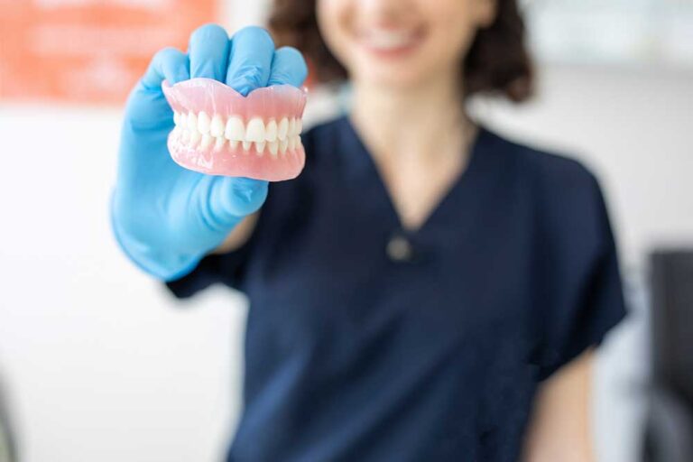 Dental professional holding a pair of dentures with blue gloves on her hand.