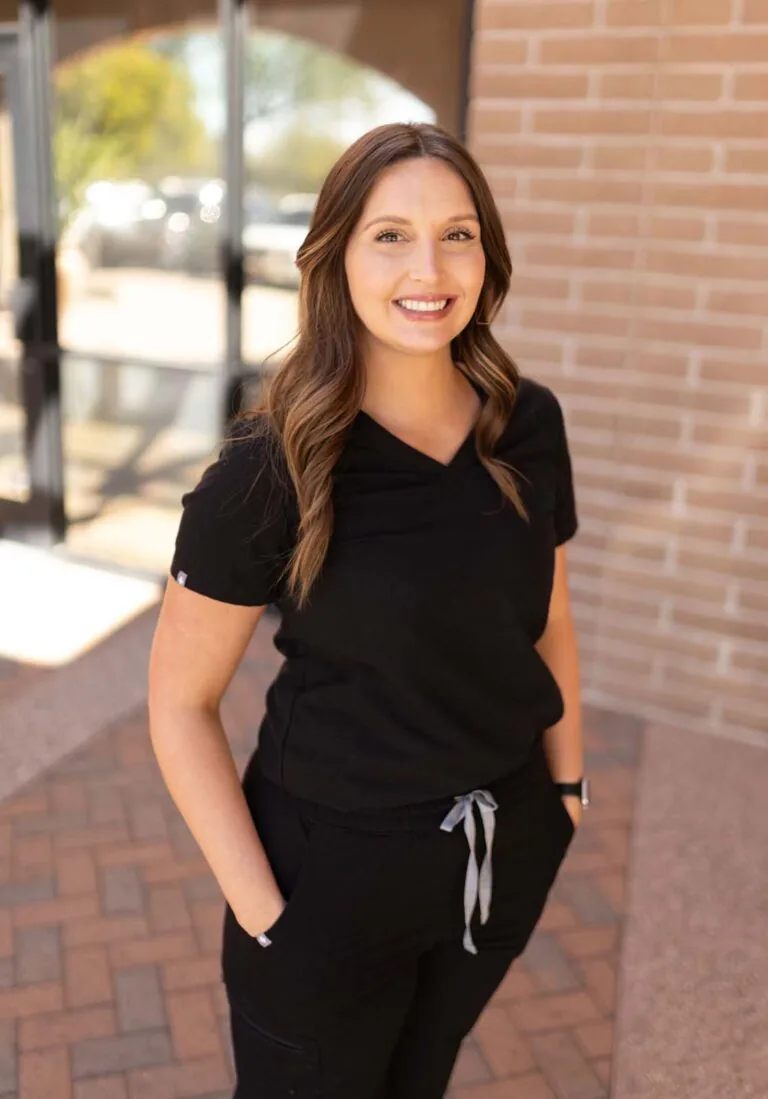 A woman standing in front of a brick wall with her both of her hands in the pockets.