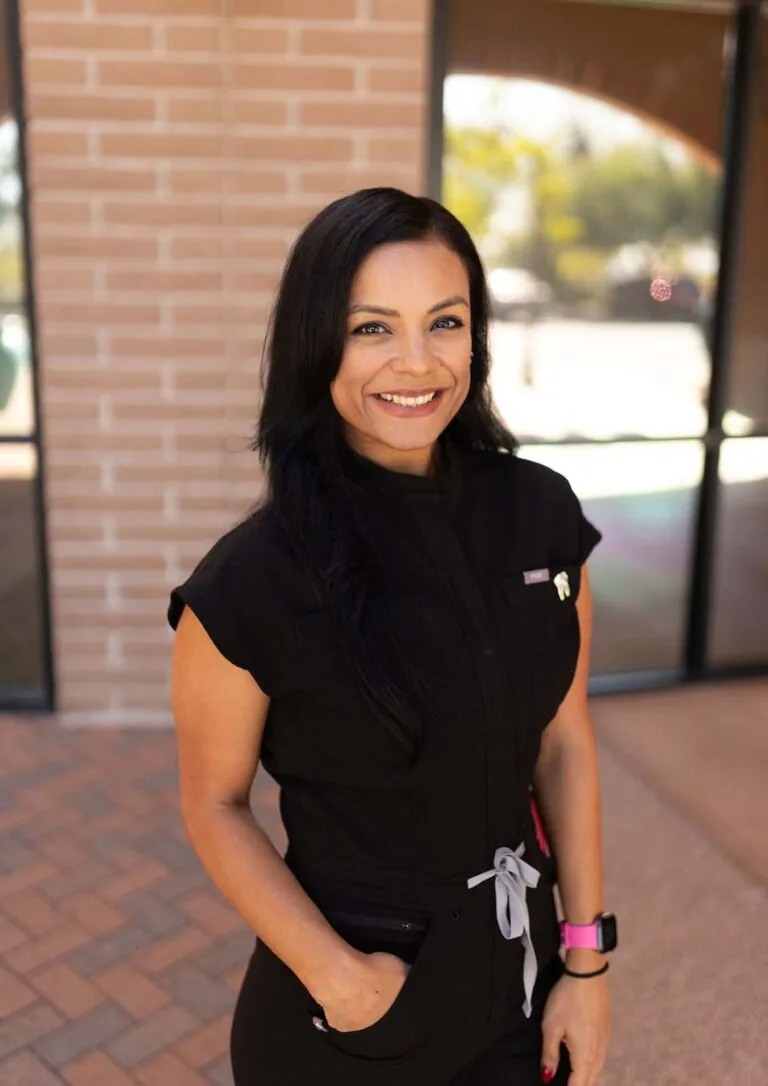 A woman wearing a black scrubs standing in front of a brick of wall with one of her hand in the pocket.