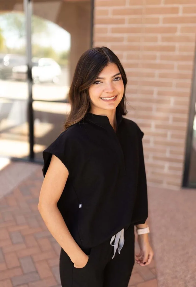 A woman standing in front of a brick wall with one of her hand in the pocket.