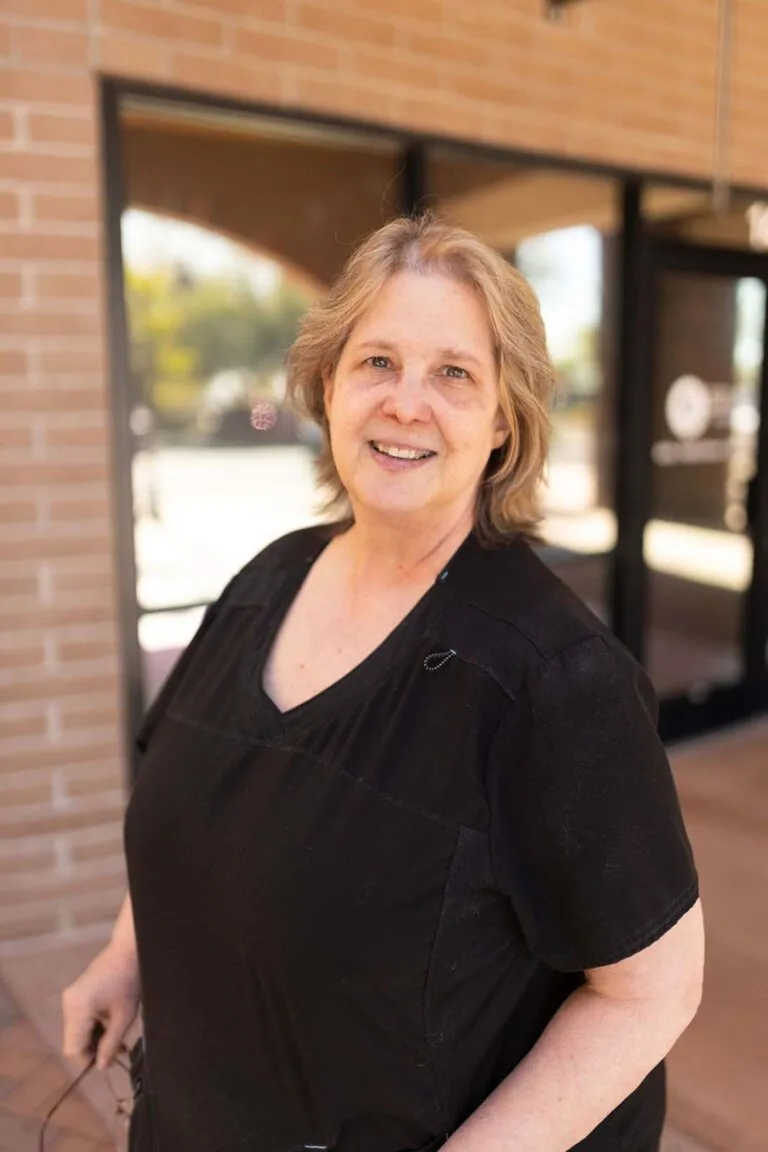 A woman wearing a black scrubs standing in front of a brick of wall while holding an eyeglass.