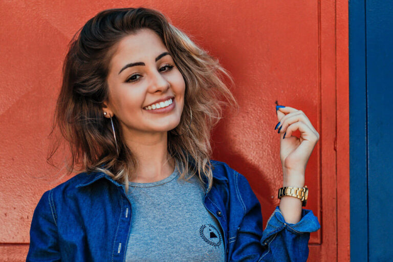 A woman smiling showing her teeth and wearing a gray shirt and a denim top.